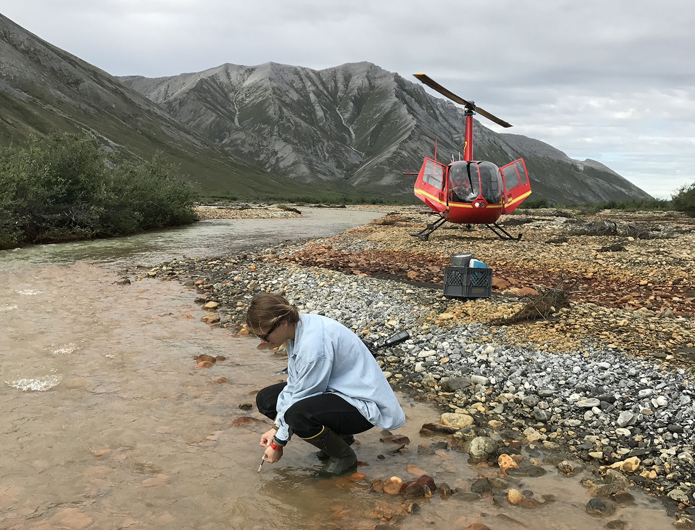 Adrianna Trusiak crouches in a river collecting iron samples