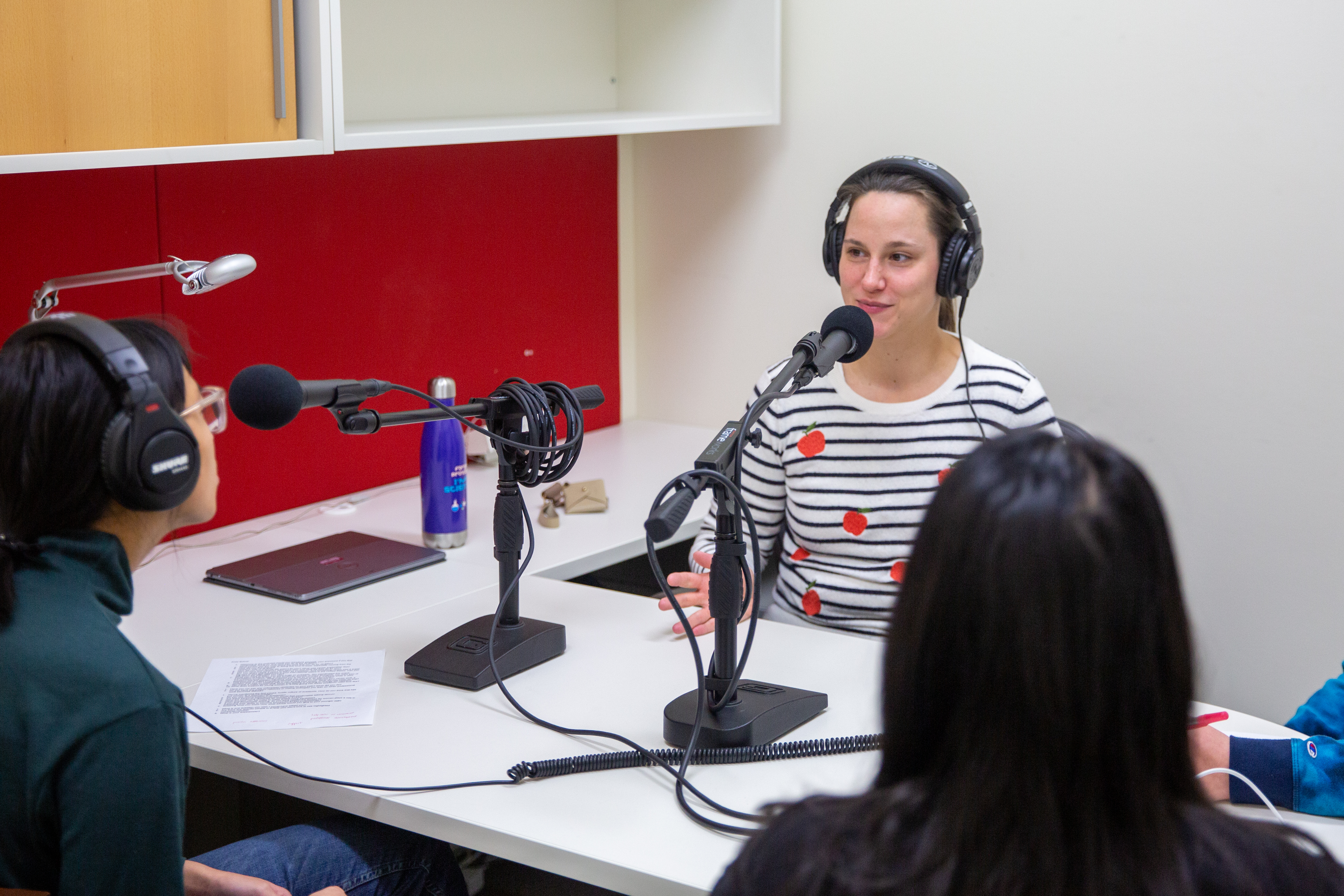 Anne-Sophie Bohrer sits behind a desk speaking into a microphone, while GLBRC communications team listens