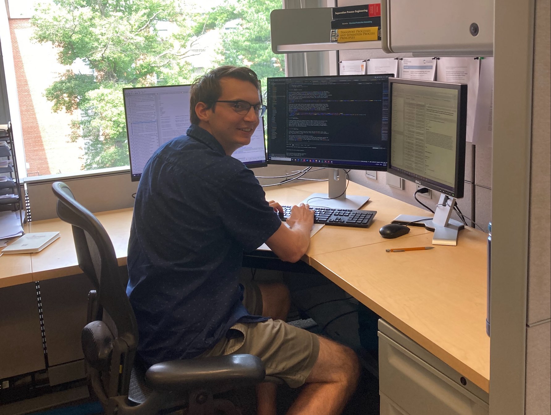 A man with short brown hair and glasses works at a computer.