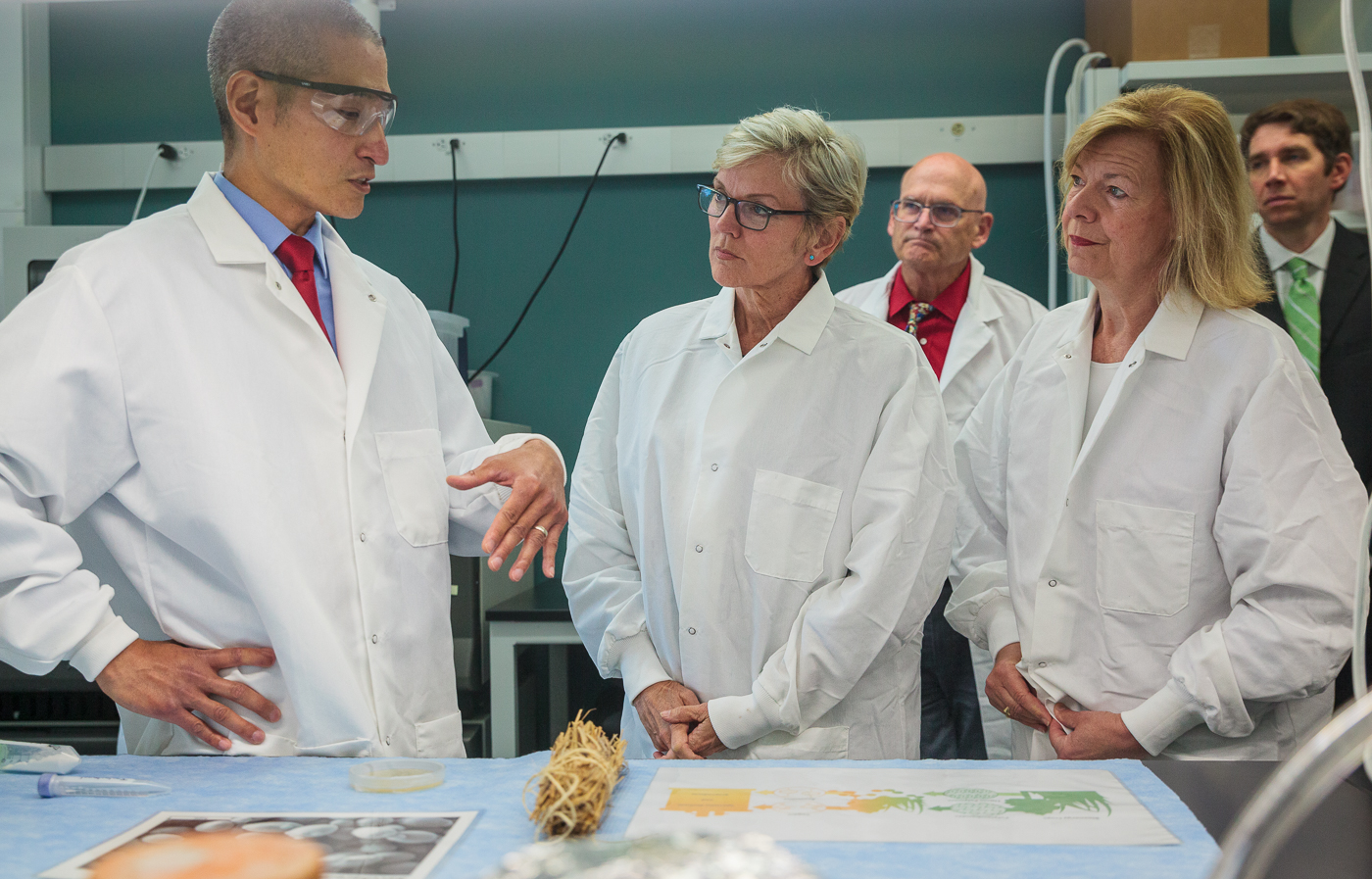 Scientist in lab coat talks to officials