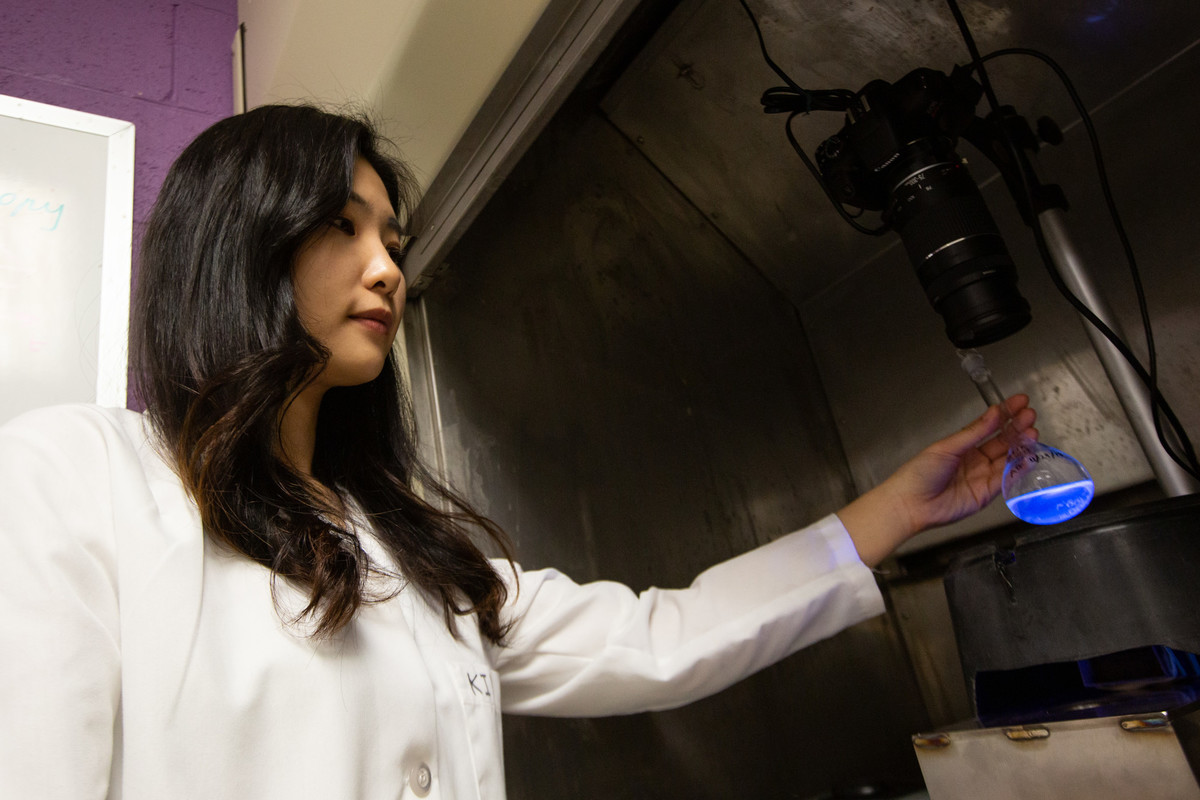 Researcher in white lab coat holds flask of glowing blue liquid