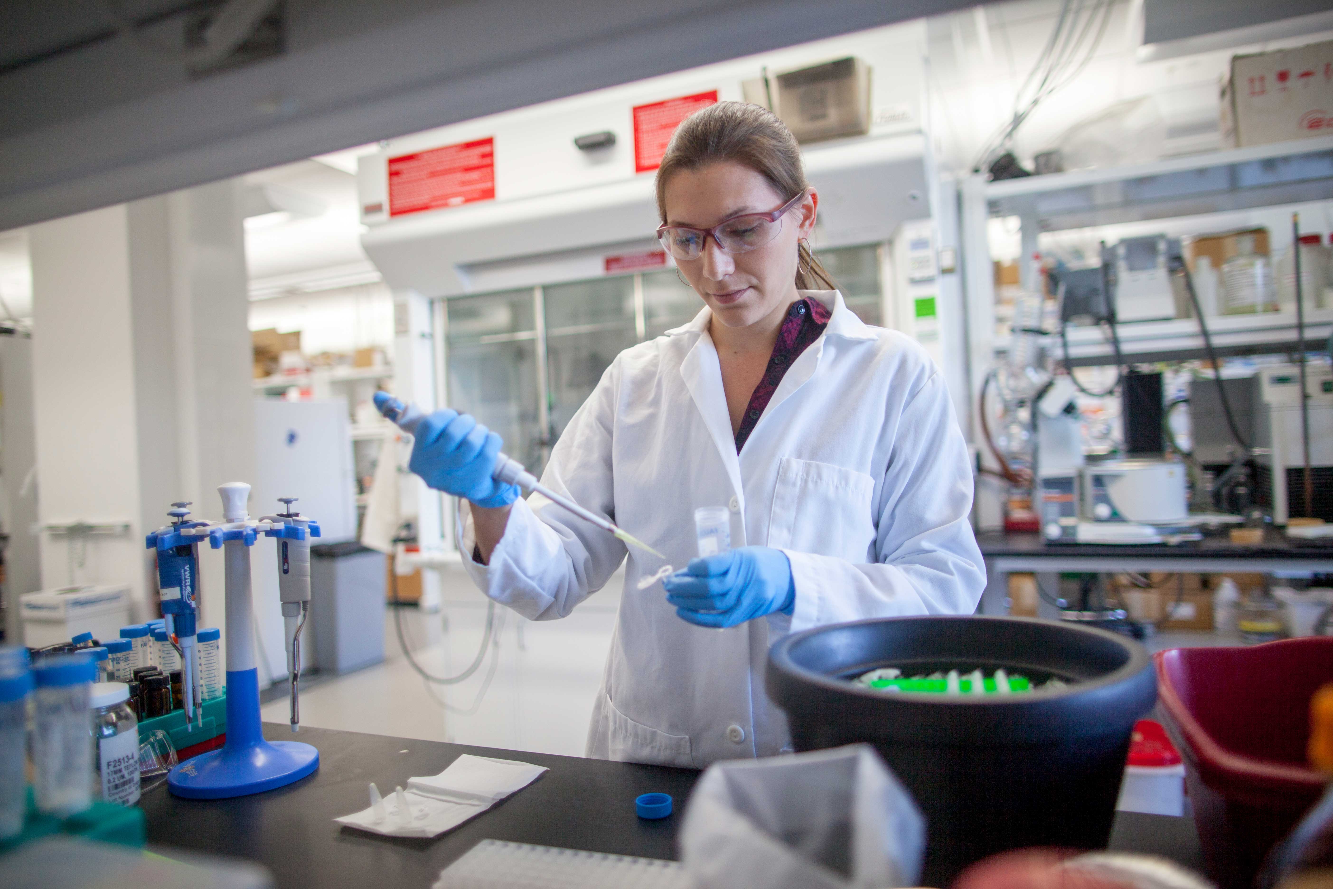 Woman in white lab coat and blue rubber gloves working at a lab bench