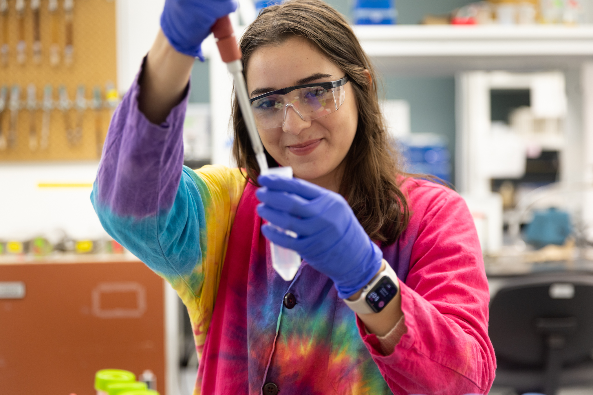 Woman with long brown hair in tie-died lab coat fills test tube