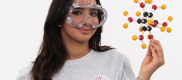 Girl wearing protective lab goggles holds a three-dimensional model of a molecule