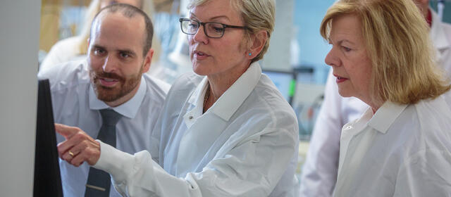 Woman in lab coat pointing to computer monitor as man and woman look on