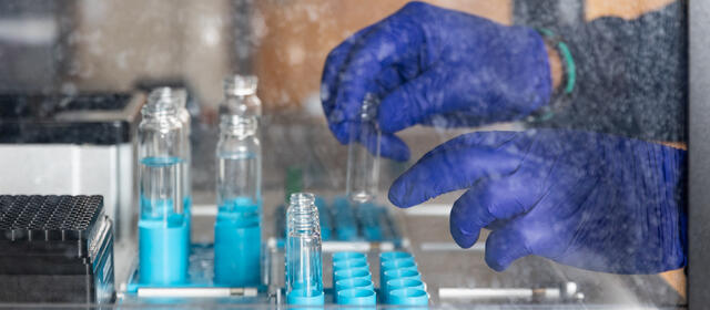 A pair of hands in blue rubber gloves put test tubes into a machine