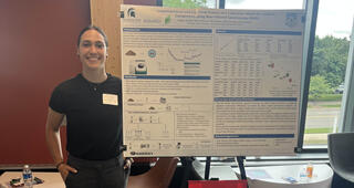 A woman with her hair pulled back into a ponytail stands in front of a science presentation poster and window