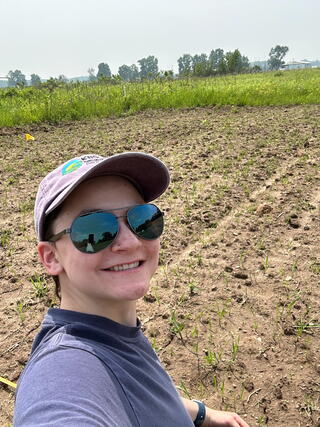 Manson in a ball cap and sunglasses takes a selfie in front of a field