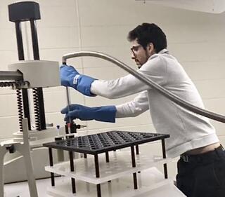 Manar Alherech filling the top of a large NMR spectrometer with liquid helium