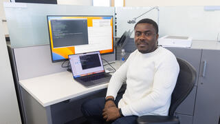 Blaise Manga Enuh sits at his desk in front of a computer screen.