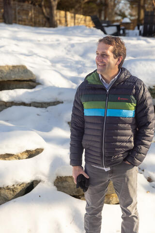 Man wearing a black coat with a blue stripe standing outside in a snow-covered landscape