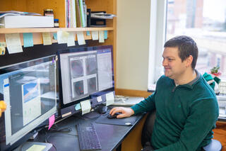 Man in green shirt sitting at desk with two computer monitors