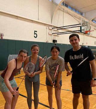 Four students holding badminton rackets posing in a gymnasium