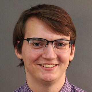 The face of a smiling man with glasses and brown hair on a gray background.