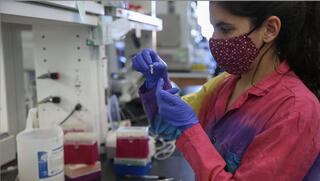 Linda, wearing a colorful labcoat and gloves, works in the lab.