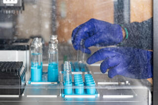 A pair of hands in blue rubber gloves put test tubes into a machine
