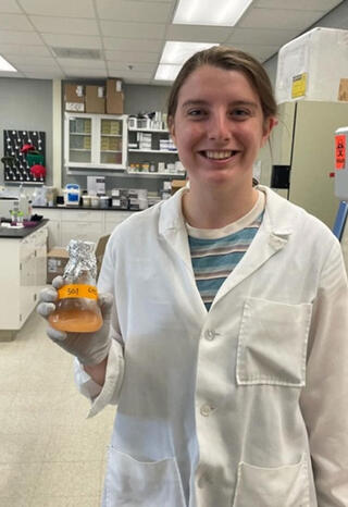 Maisie Smith holds a beaker containing orange liquid.
