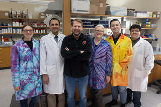Six people pose for a photo in a lab
