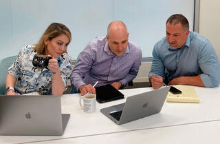 A woman and two men seated at a table look at a laptop computer screen