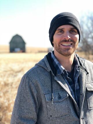 Tyler Lark stands in a field with a barn visible in the distance