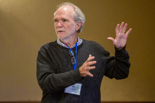 Man in dark sweater gestures while speaking