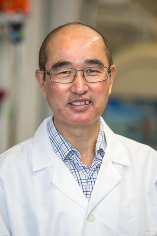 Asian man with short-cropped hair and glasses in white lab coat