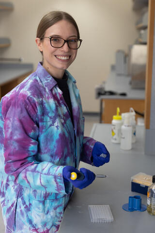 Smiling woman in tie-died lab coat and blue rubber gloves