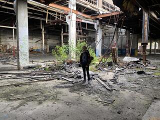 Ben Bridge, a young man in a sweatshirt and jeans, stands in an abandoned paper mill.