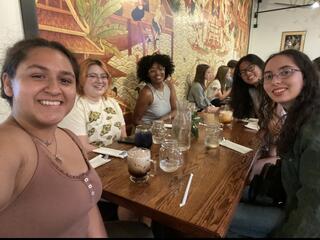 Five students sit at a restaurant table smiling.