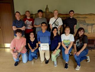 Salvador Castillo holds up a certificate while kneeling on the ground surrounded by his colleagues.