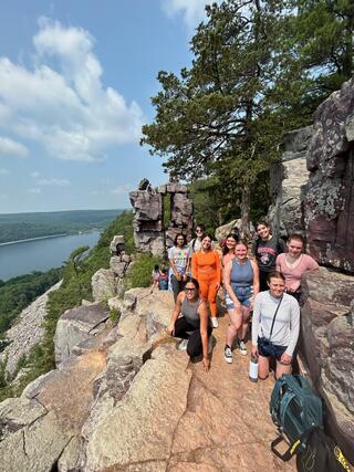 A group of young students stand on a rocky path with views overlooking a lake.