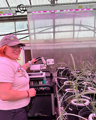 Veronica Pargulski stands under the red lights in a greenhouse