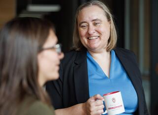 Woman in blue shirt holds a coffee mug and looks at another woman in the foreground