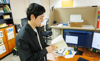 Man leafing through a notebook while standing at a work cubicle