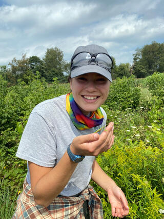 Woman in gray T-shirt and baseball cap holds a green mantis