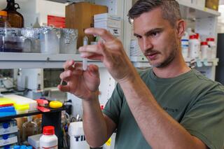A researcher closely examines a small microcentrifuge tube in a molecular biology laboratory.